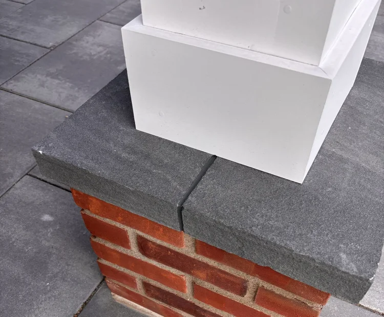 Dark sealant at the stone-cap joint beside white column trim.