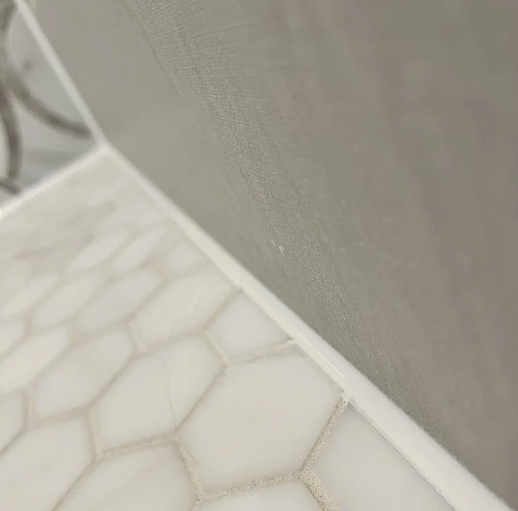 Continuous white sealant at the wall-to-hexagonal-tile junction.