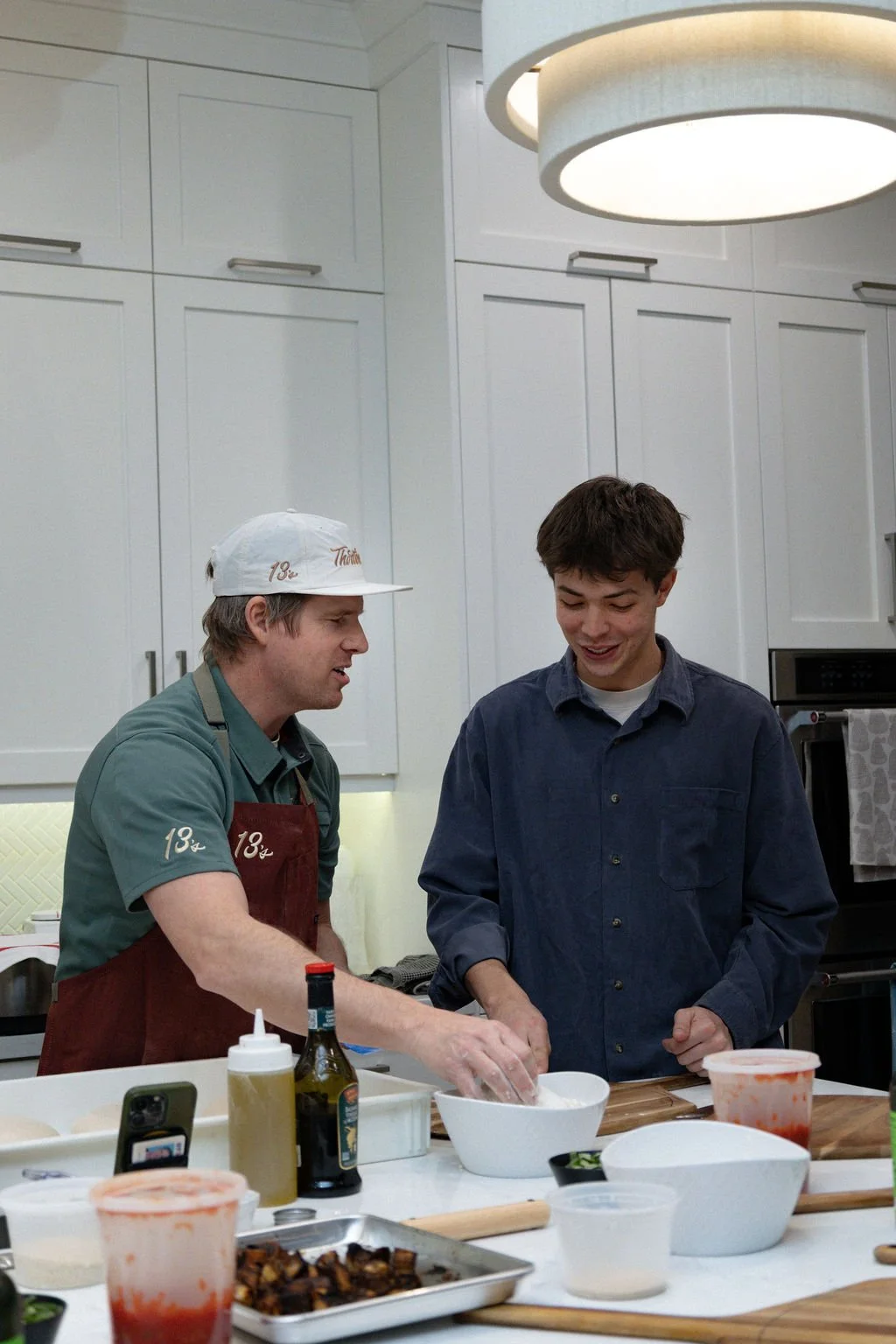 Chef Mark teaching a guest to build a pizza at a hands-on pizza class