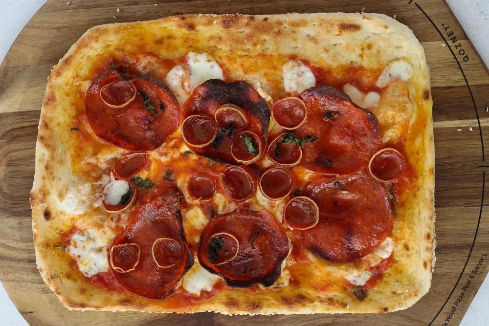 Whole rectangular Grandma-style pepperoni pizza on a wooden board