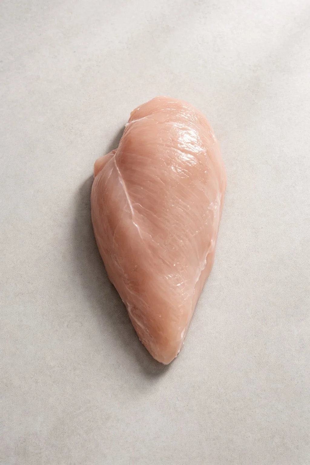 A raw chicken breast on a light gray surface