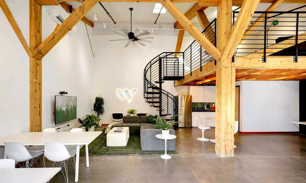 Inside the Works Real Estate Bend office, with exposed timber beams, welcoming seating, and a spiral staircase.