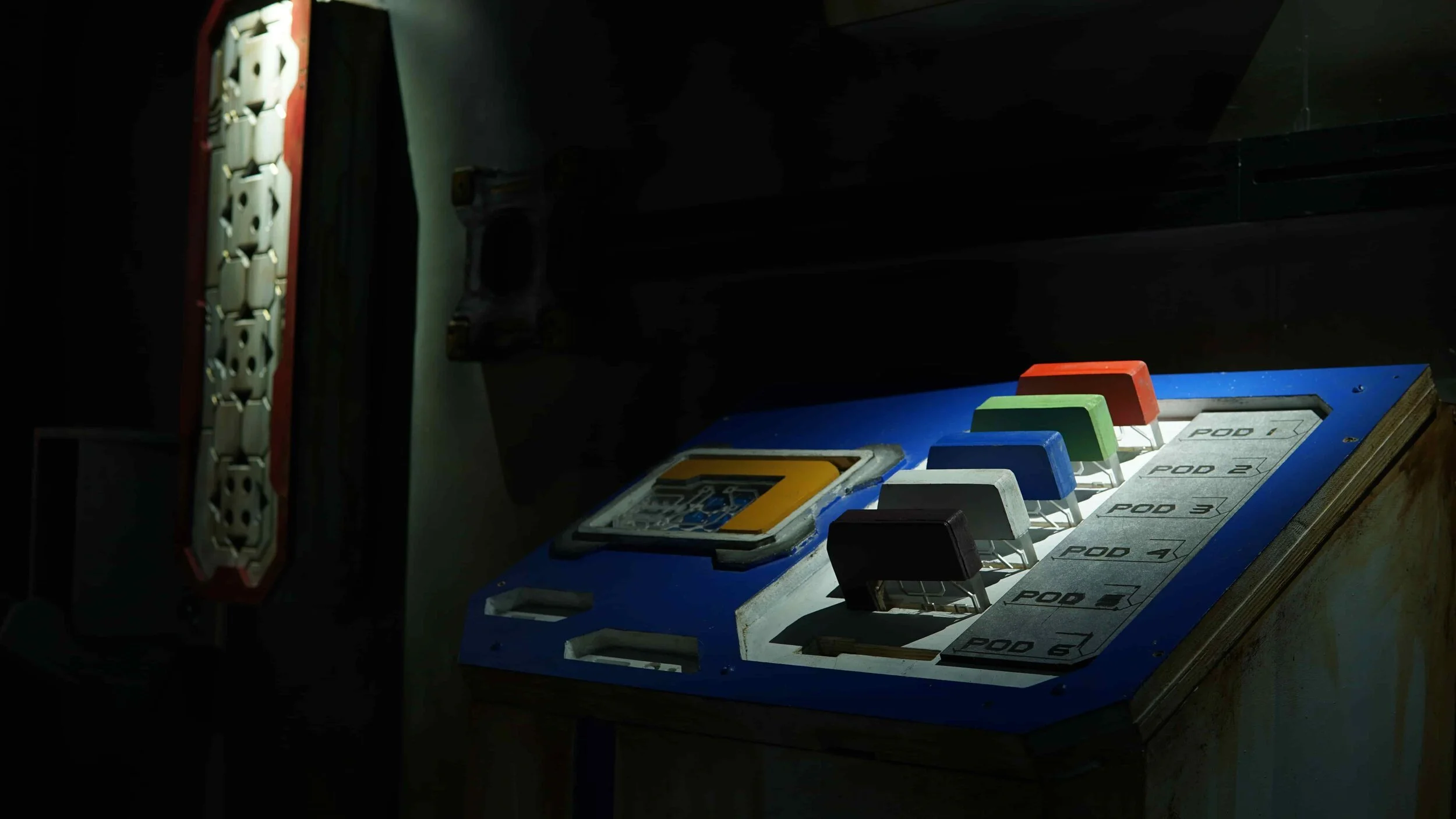 Sci-fi control panel with colored switches and ‘POD’ labels in a dark escape room.