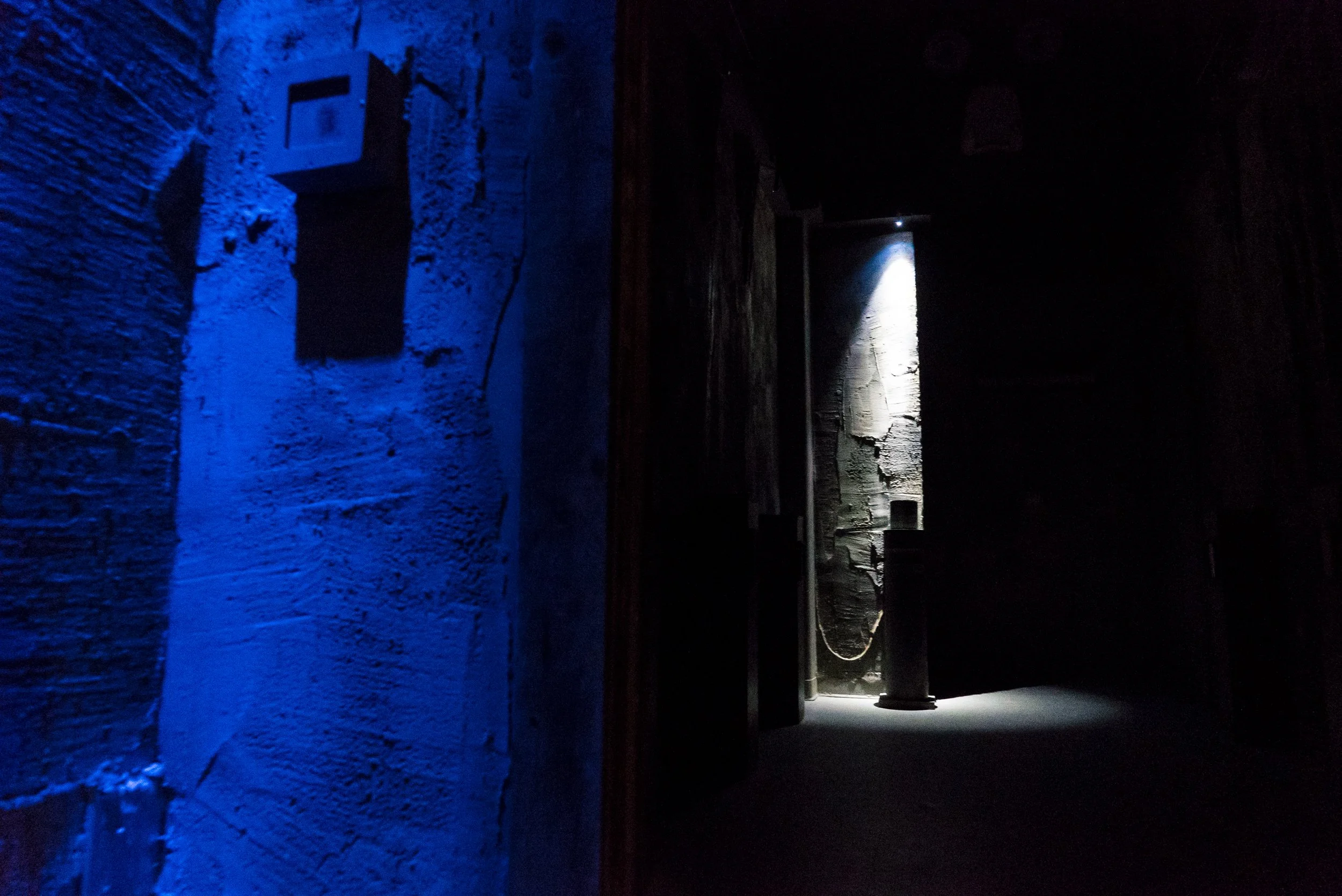 Dim concrete corridor washed in blue light with a spotlighted alcove at the far end.
