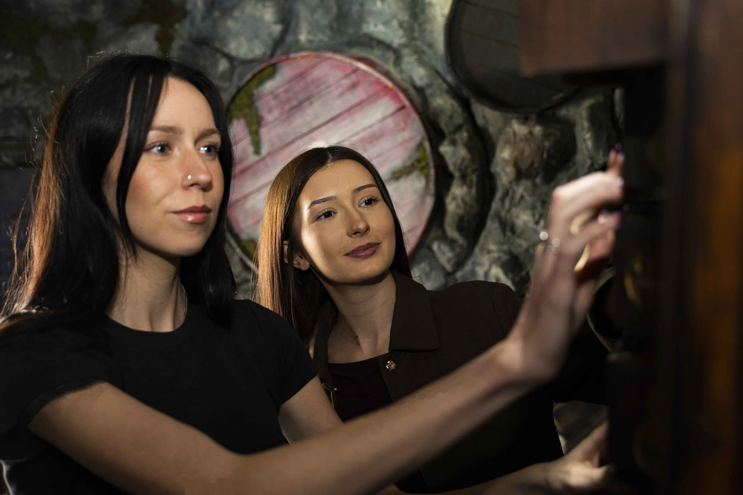 Two players operating a wall-mounted mechanism inside a rock-walled pirate cave escape room.