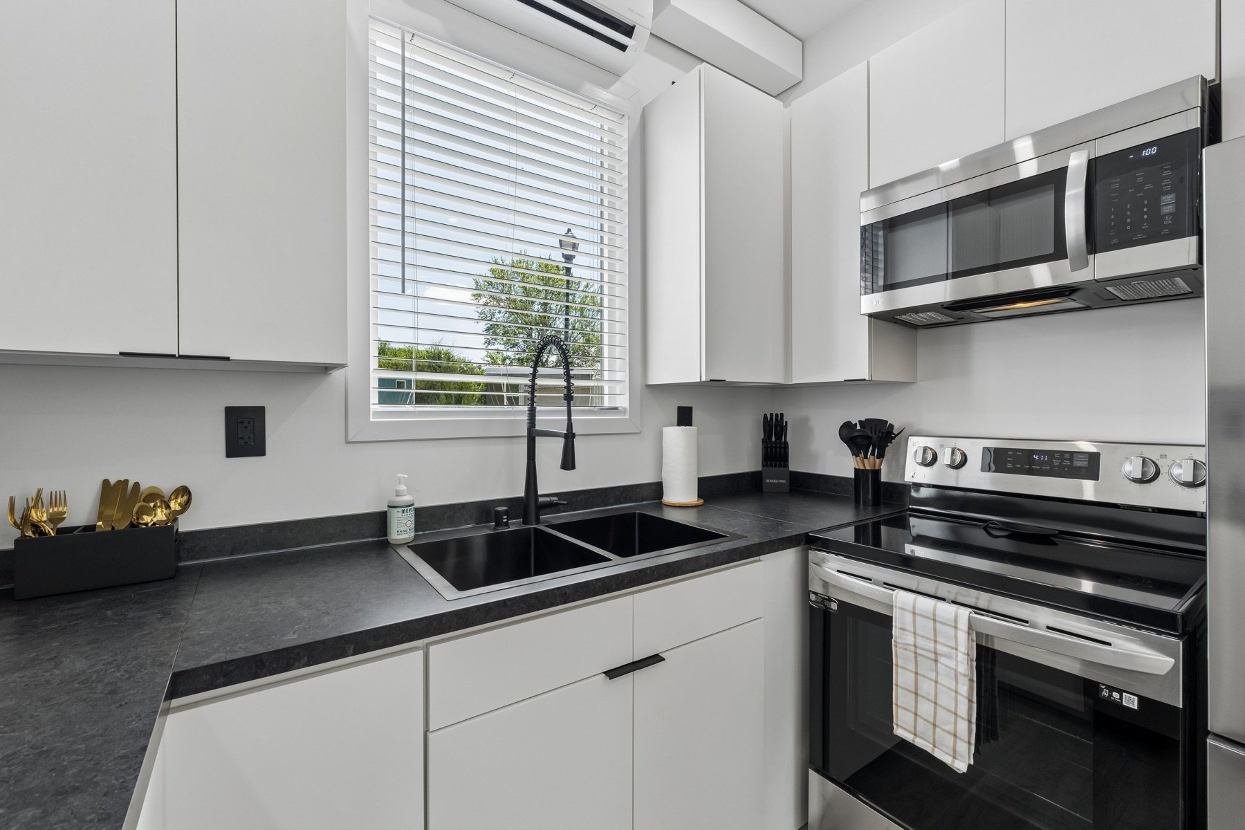 Pasadera kitchen with stainless appliances, white cabinetry and a sink below the window