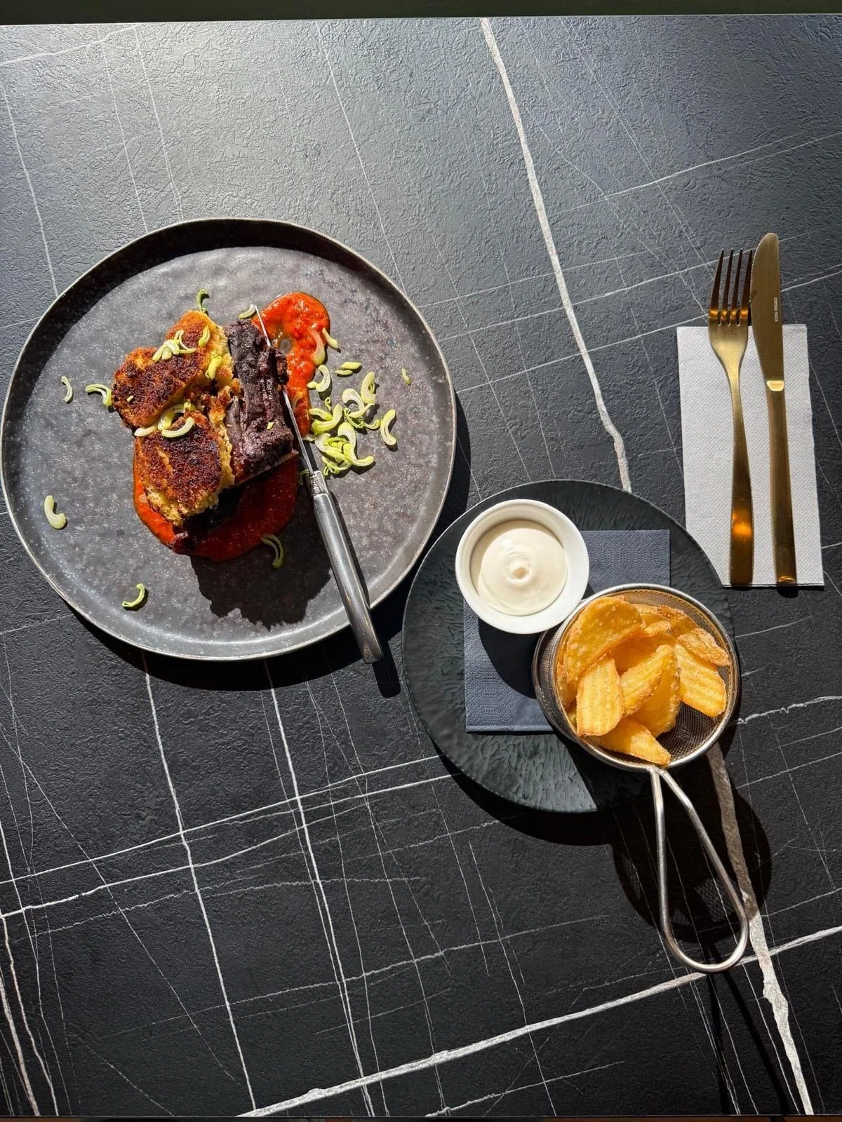 Gericht mit Paprikasauce und Pommes auf einem Bistro-Tisch aus dunklem Marmor