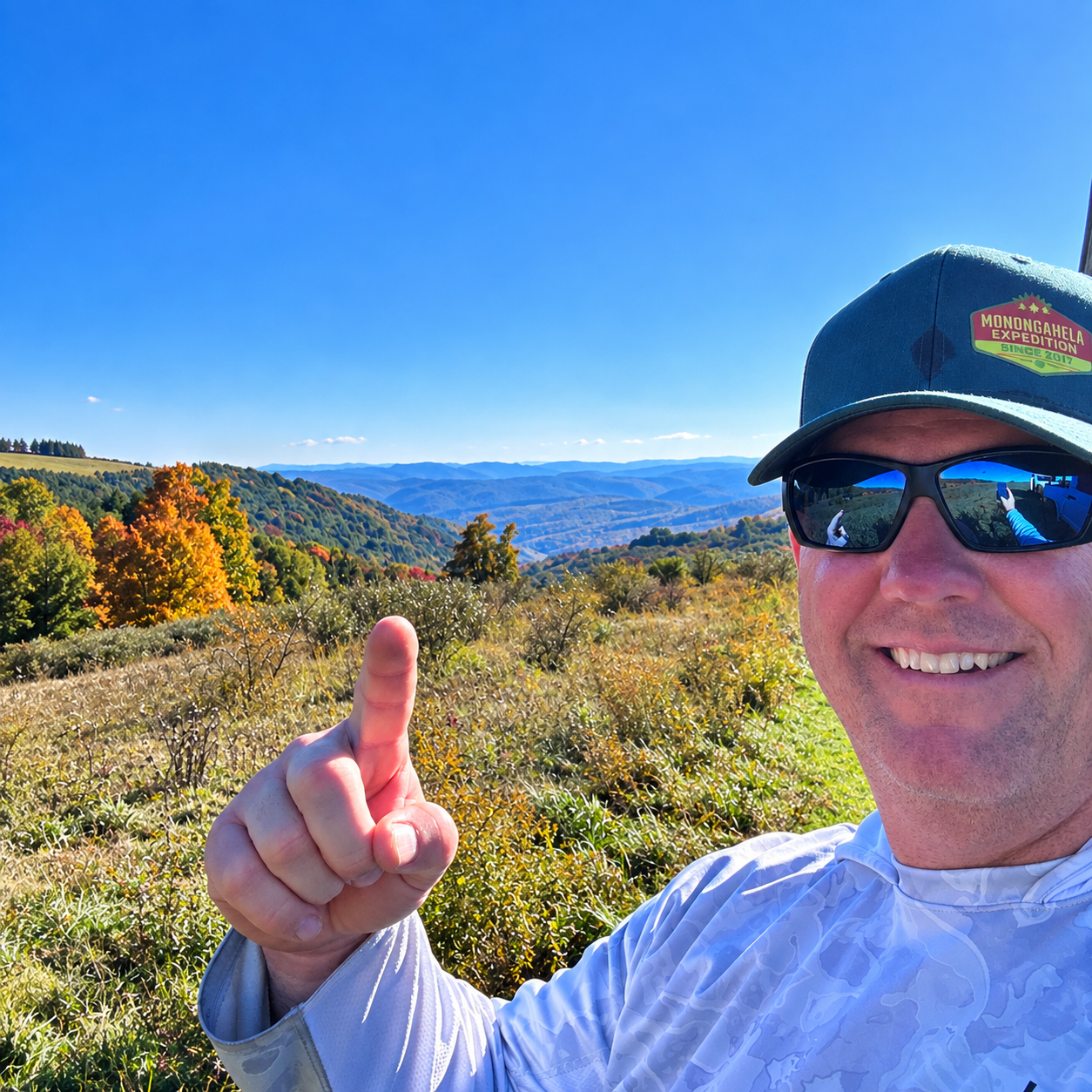 Venture To See's Don Sallee in a Monongahela Expedition hat with fall color and layered blue ridgelines behind him at Spruce Knob Mountain Center, West Virginia