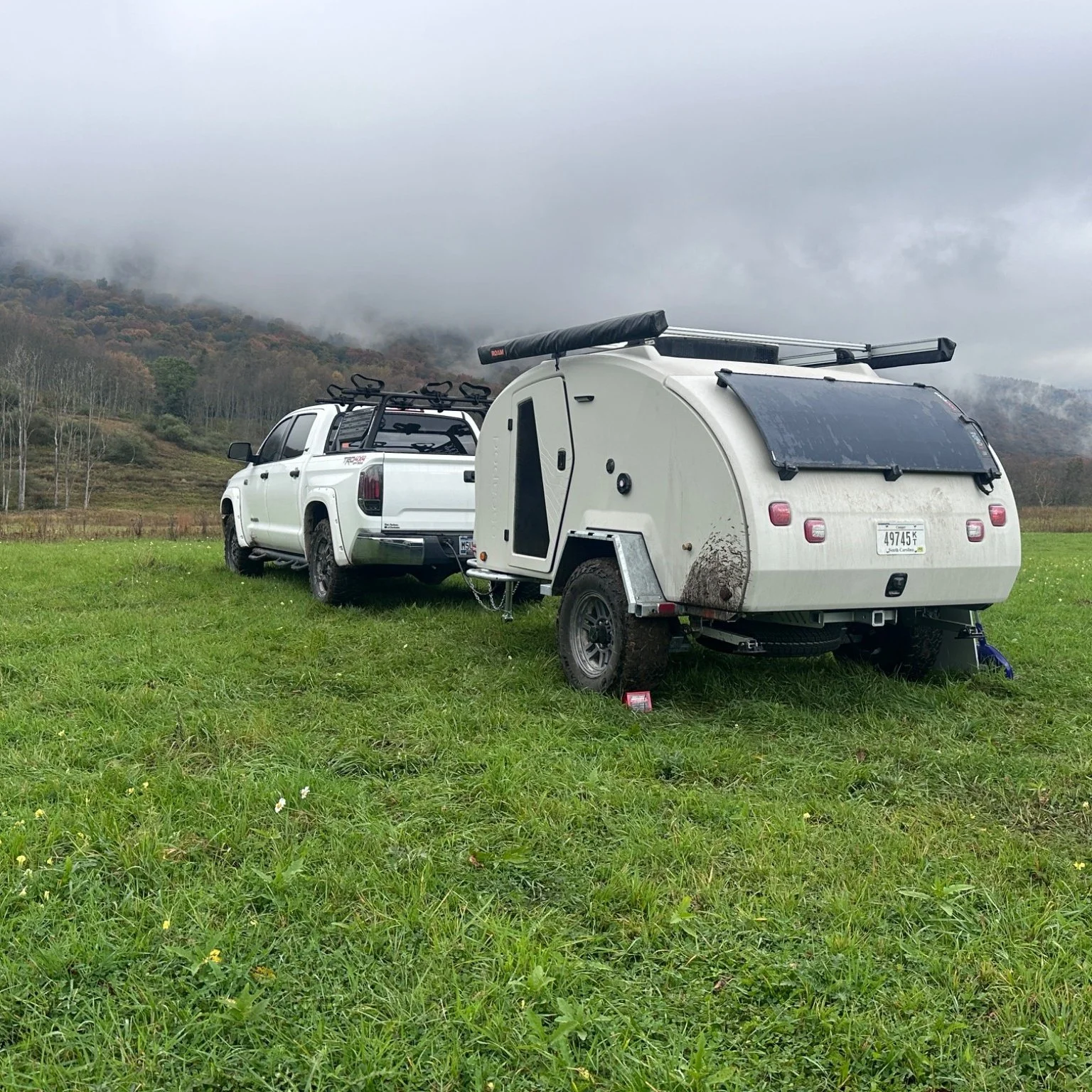 Toyota Tundra and mud-splashed Escapod Topo 2 parked in a green meadow under low clouds and fall color at Canaan Valley Resort State Park, West Virginia