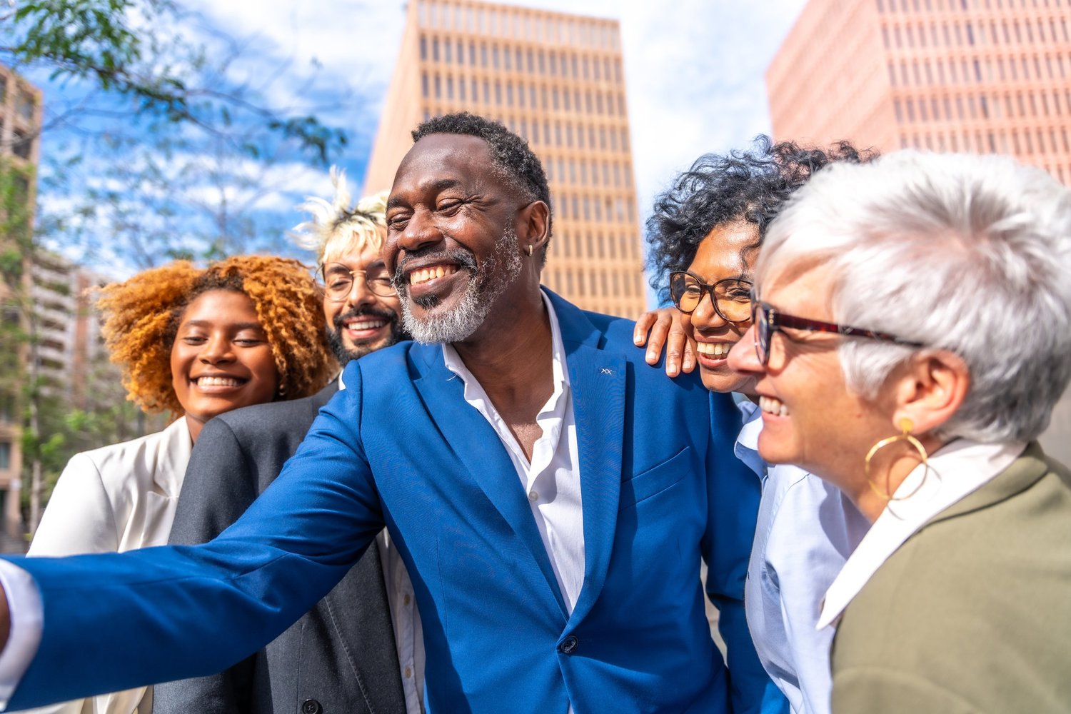 A group of adults smiling together for a selfie outdoors