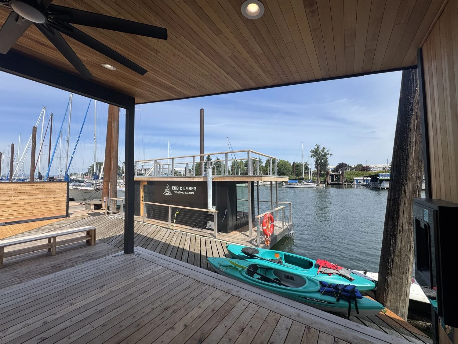 Ebb & Ember floating sauna viewed from a covered cedar deck with two teal kayaks in the foreground on the Columbia River