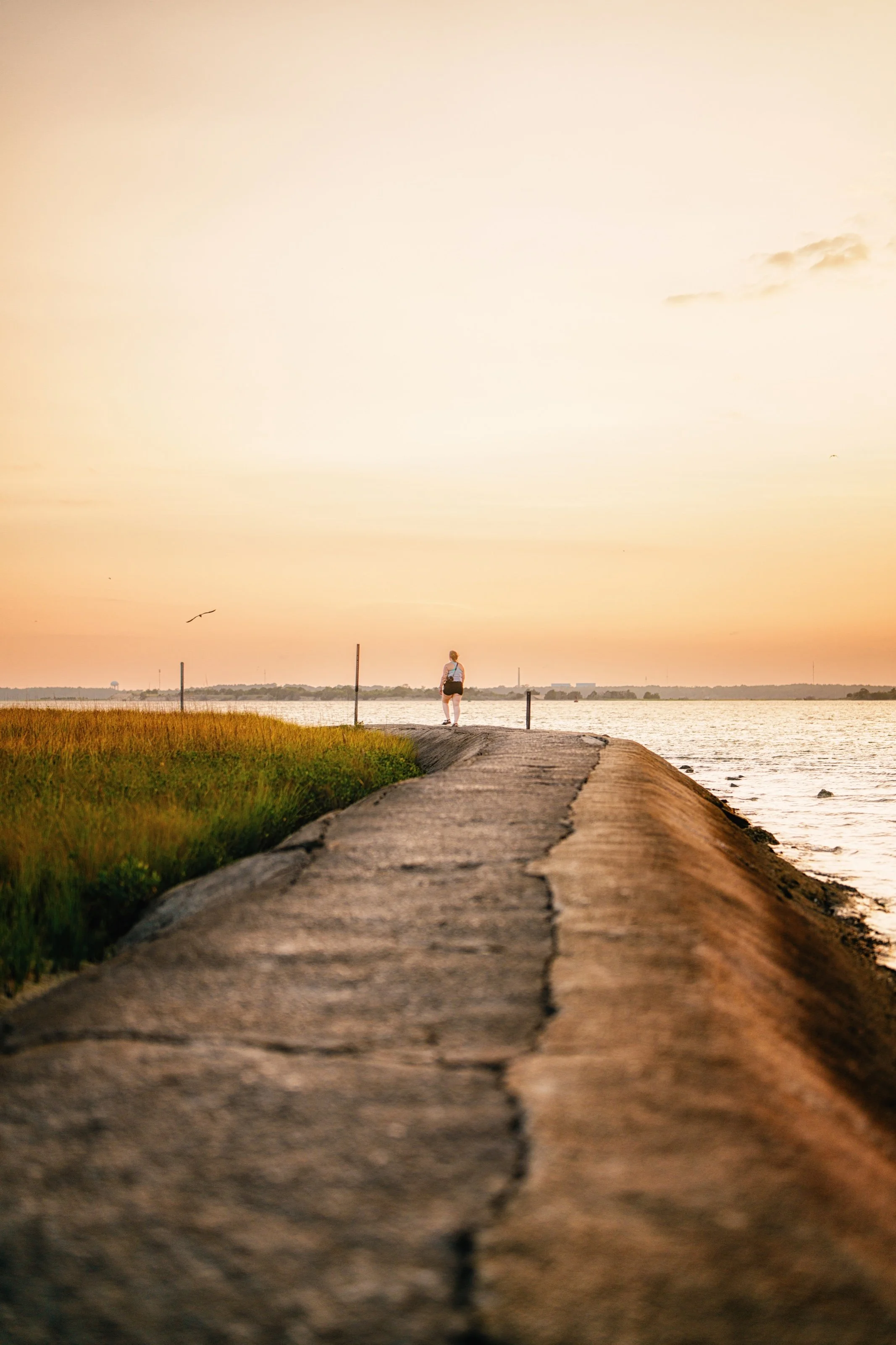 A lone figure at the end of a shoreline path in evening light