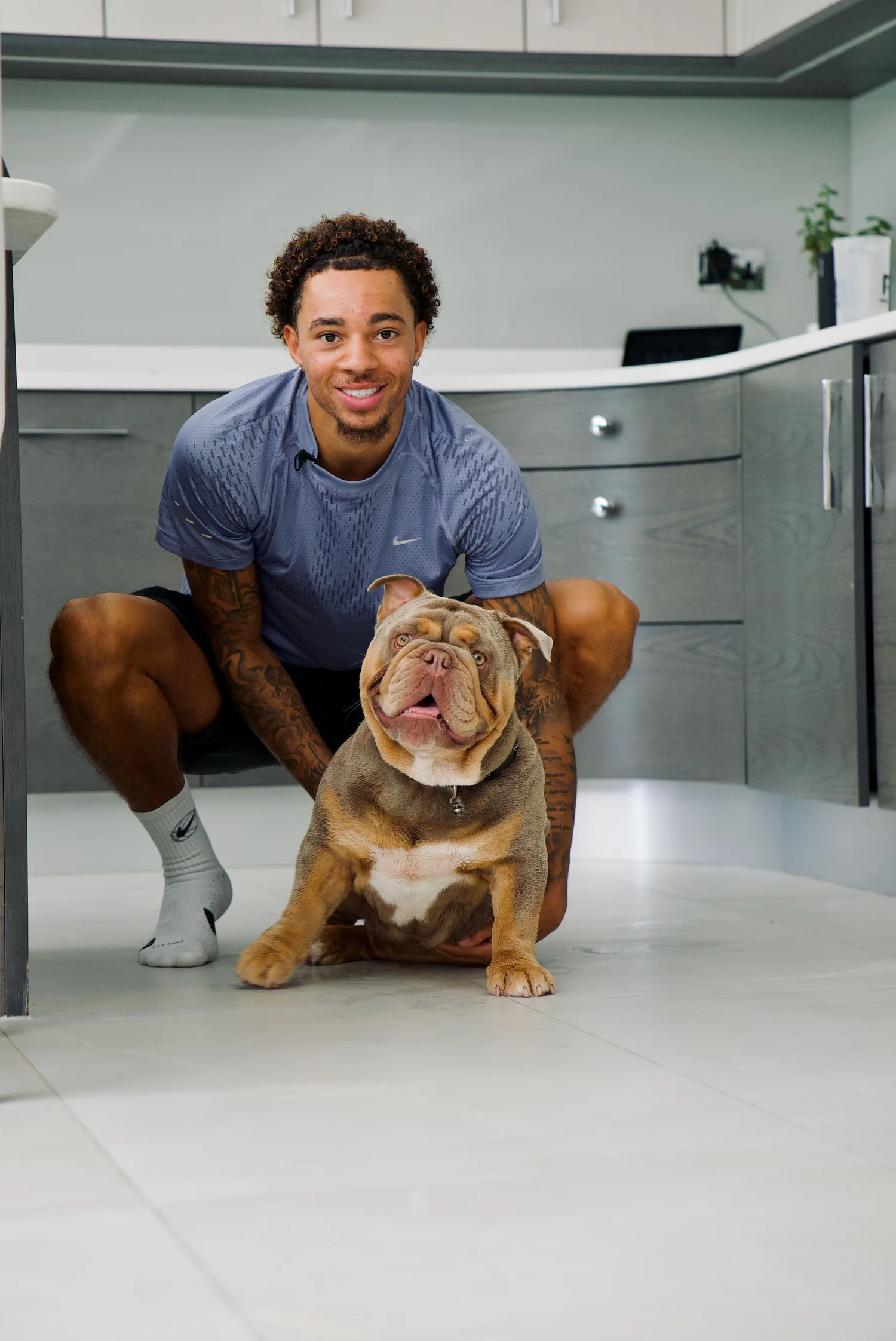 Owner crouching beside his calm bulldog in the kitchen