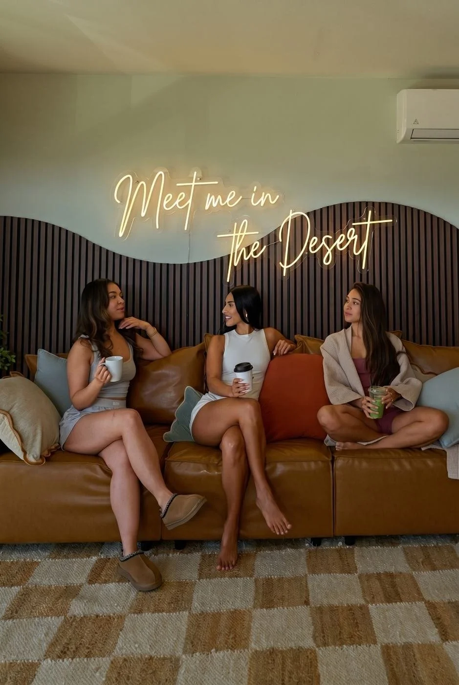 Friends on the sectional under the neon sign in the living room at The Desert Willow Joshua Tree