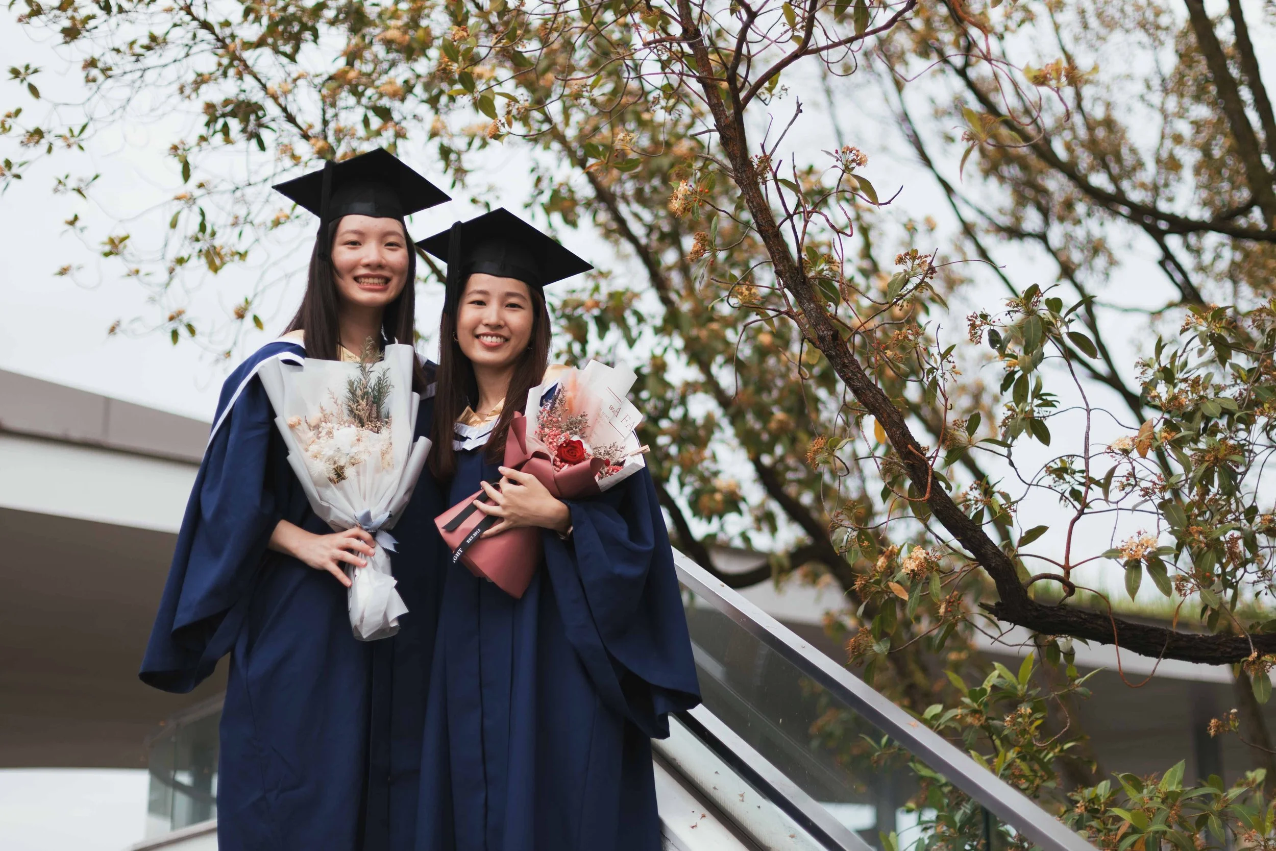 Nic and Sim walking together in graduation gowns during a photoshoot on the NUS campus in Singapore