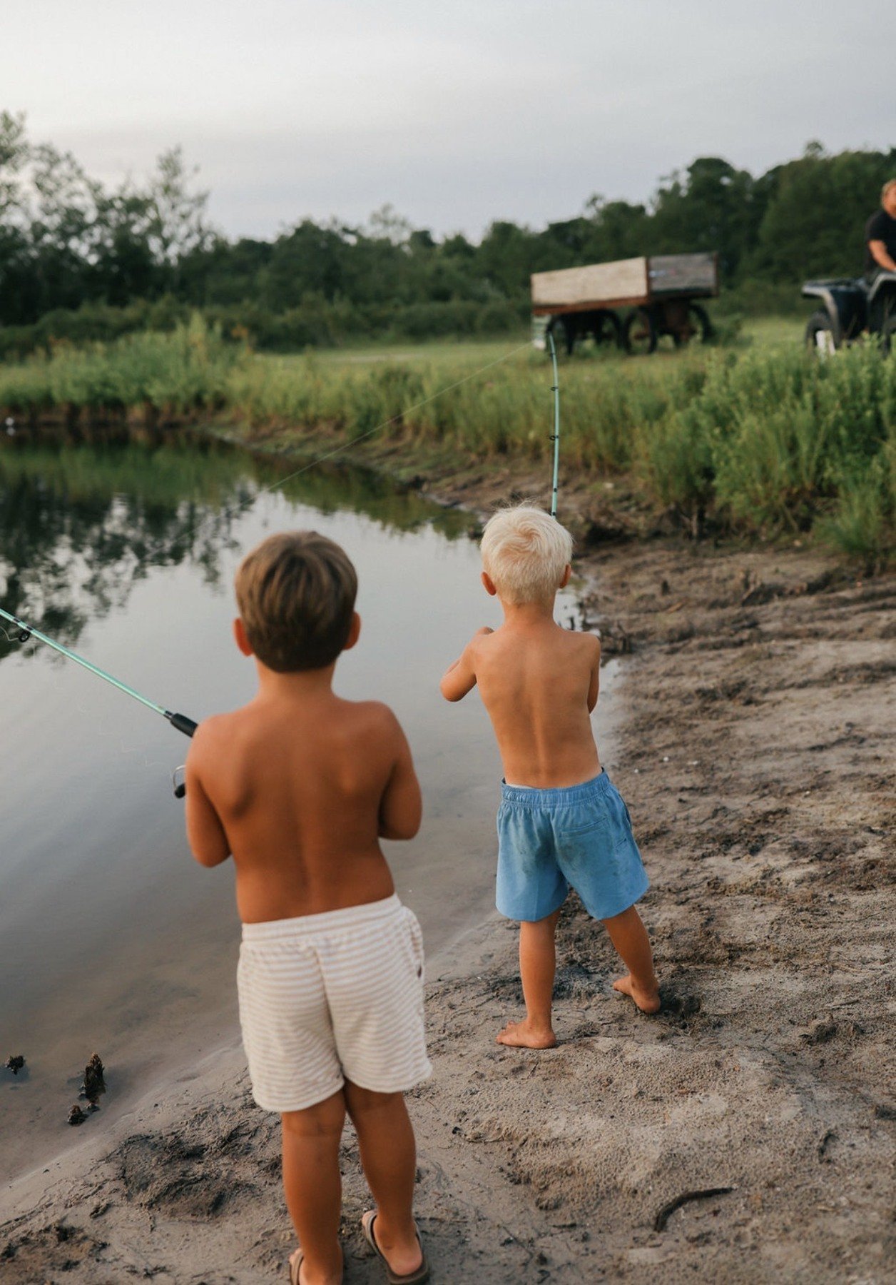 Two boys fishing beside the pond with the Bluebird Farm wagon beyond