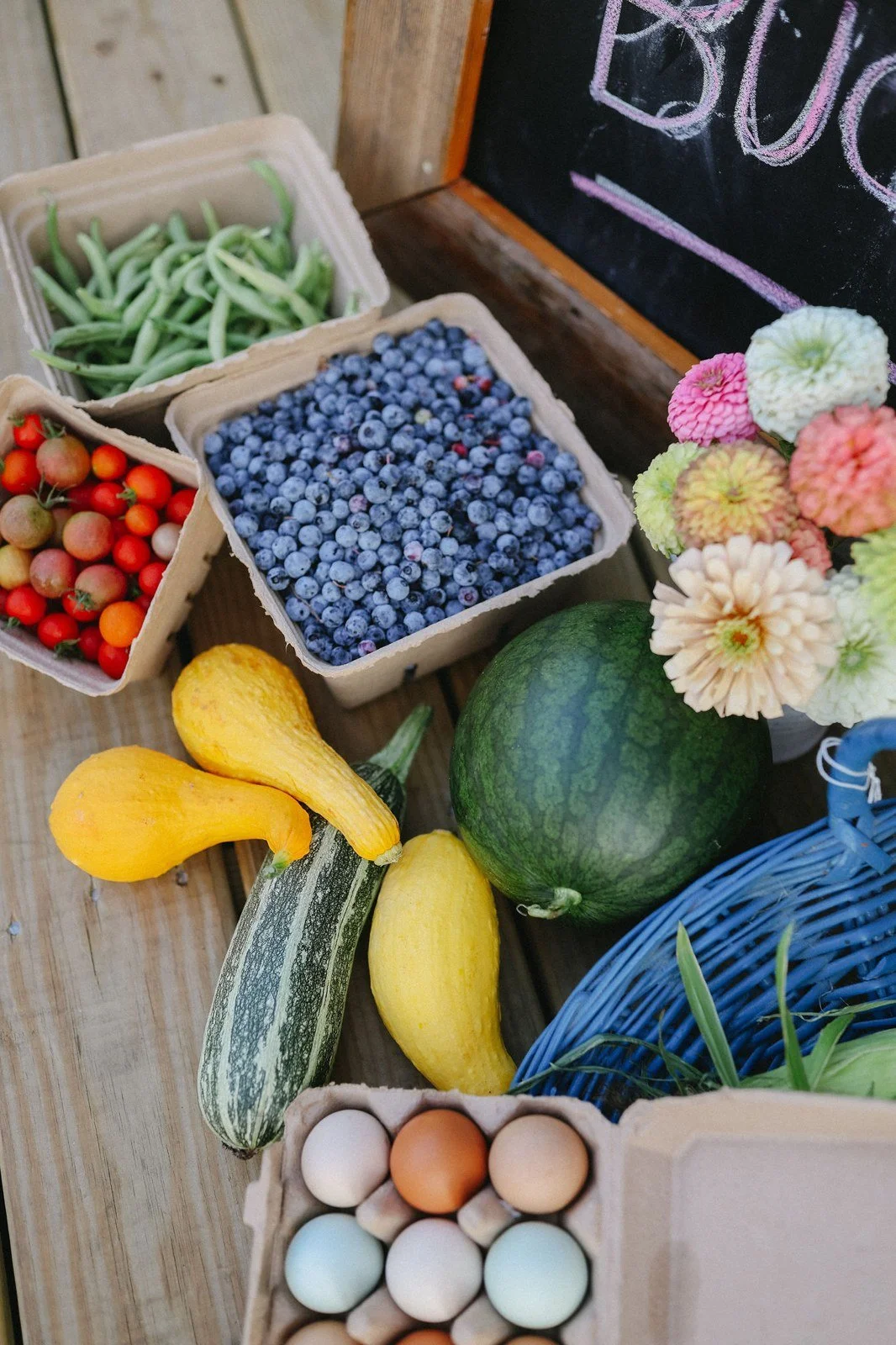 A basket of blueberries, fresh vegetables, eggs and cut flowers at Bluebird Farm