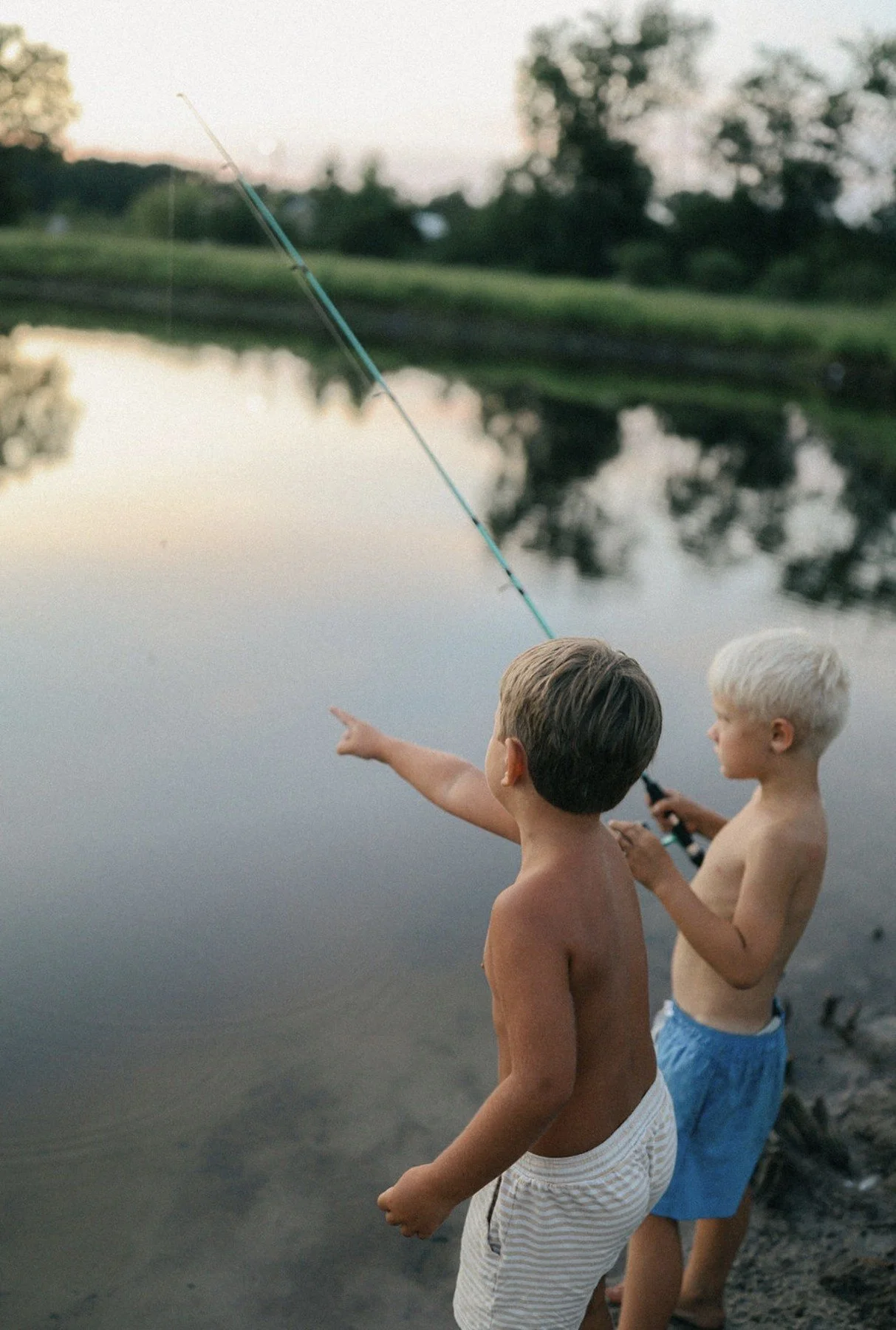 Two boys fishing together beside the pond