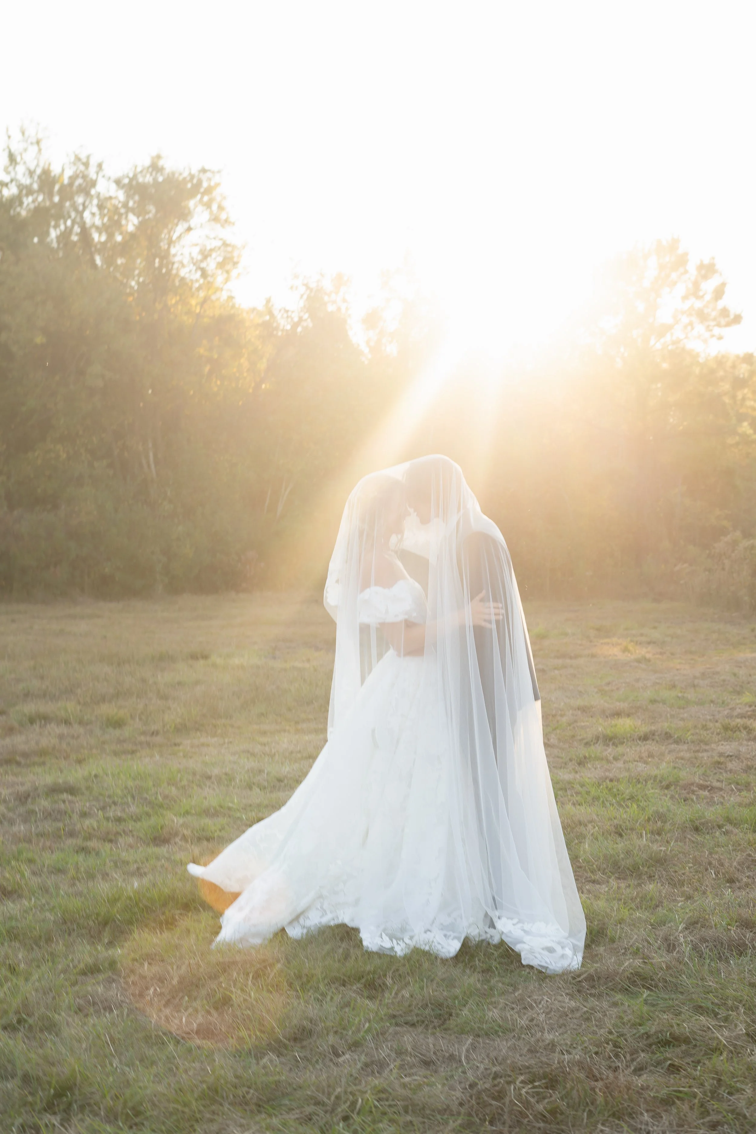 Bride and groom beneath a veil at sunset
