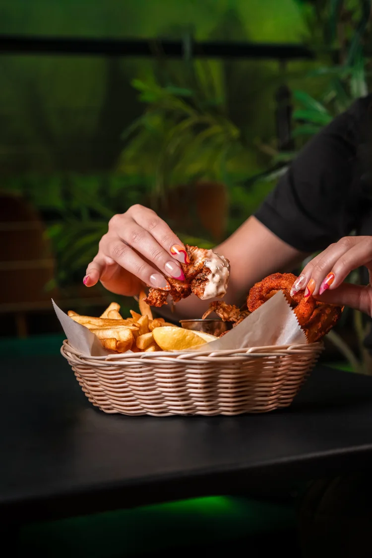 Hands pulling apart fried chicken from a basket with fries