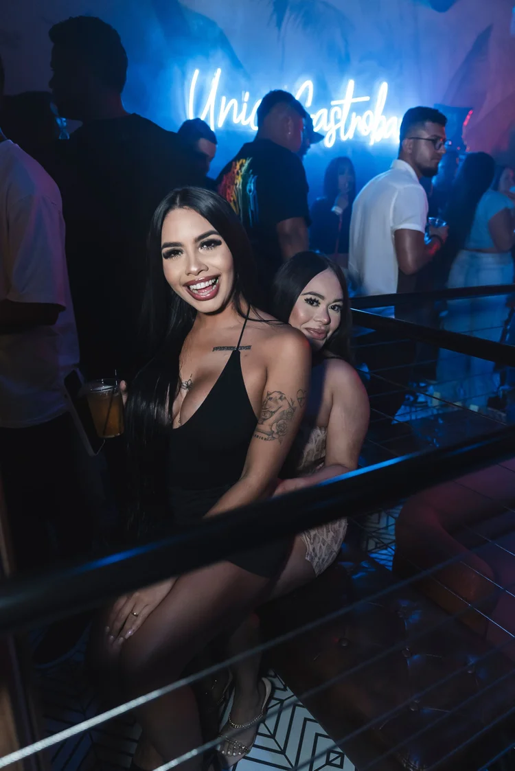 Two guests posing by the railing with the neon Unico sign behind them