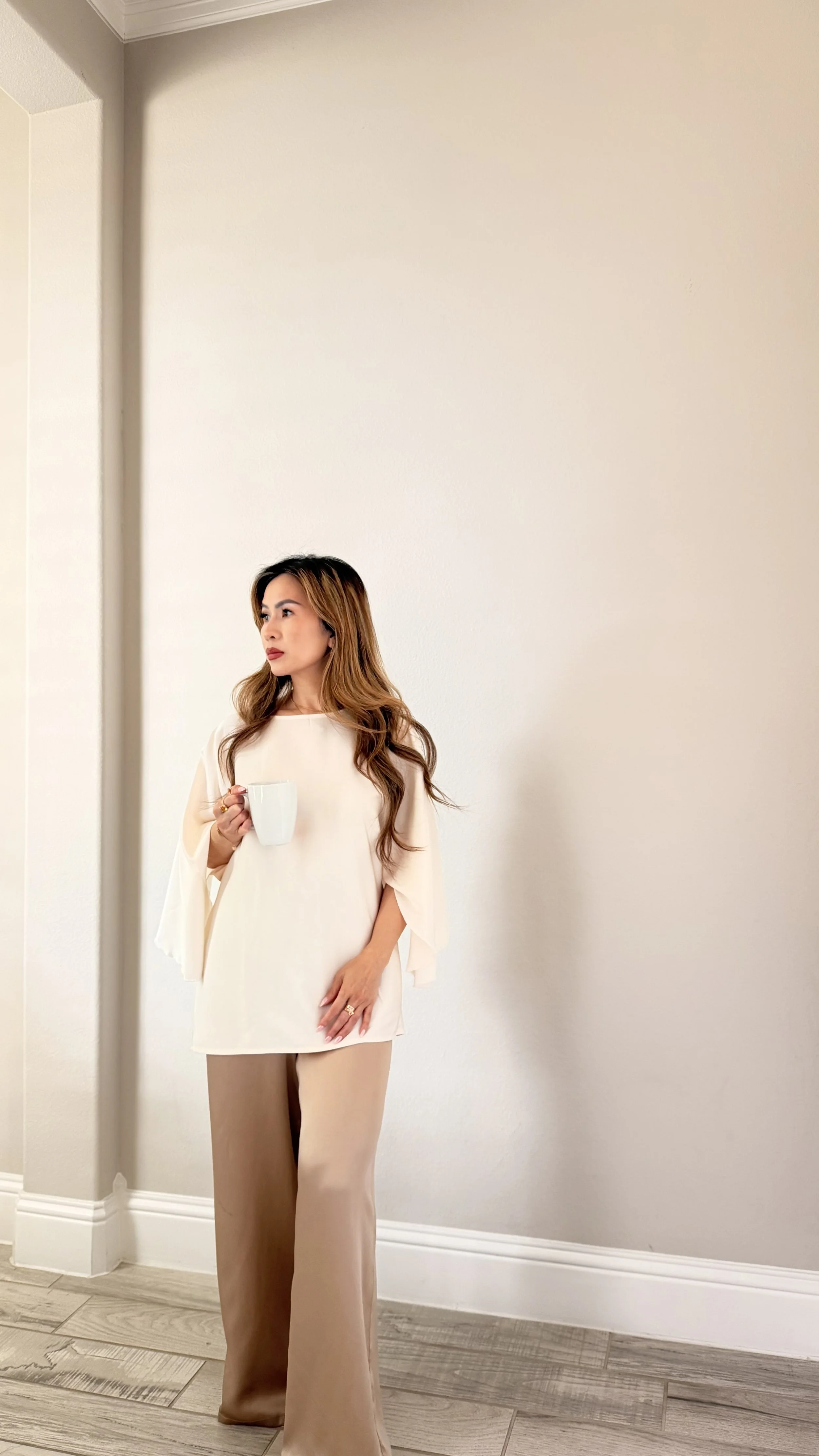 Mary Nguyen, founder and chair of HOM, standing against a white wall holding a cup.