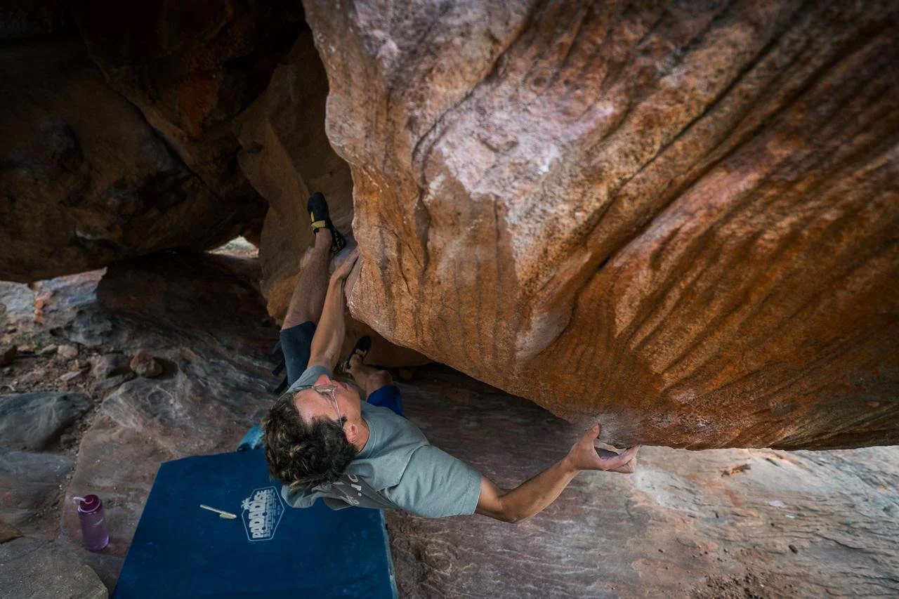 Jackson Wetherill climbing out a sandstone roof above a crash pad in Rocklands