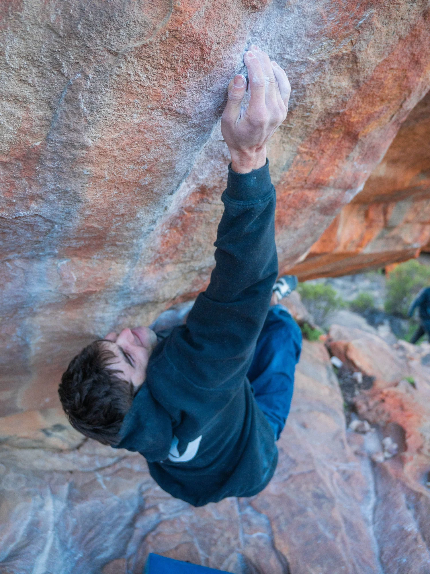 Kieran Hadley reaching up a steep orange sandstone boulder in Rocklands