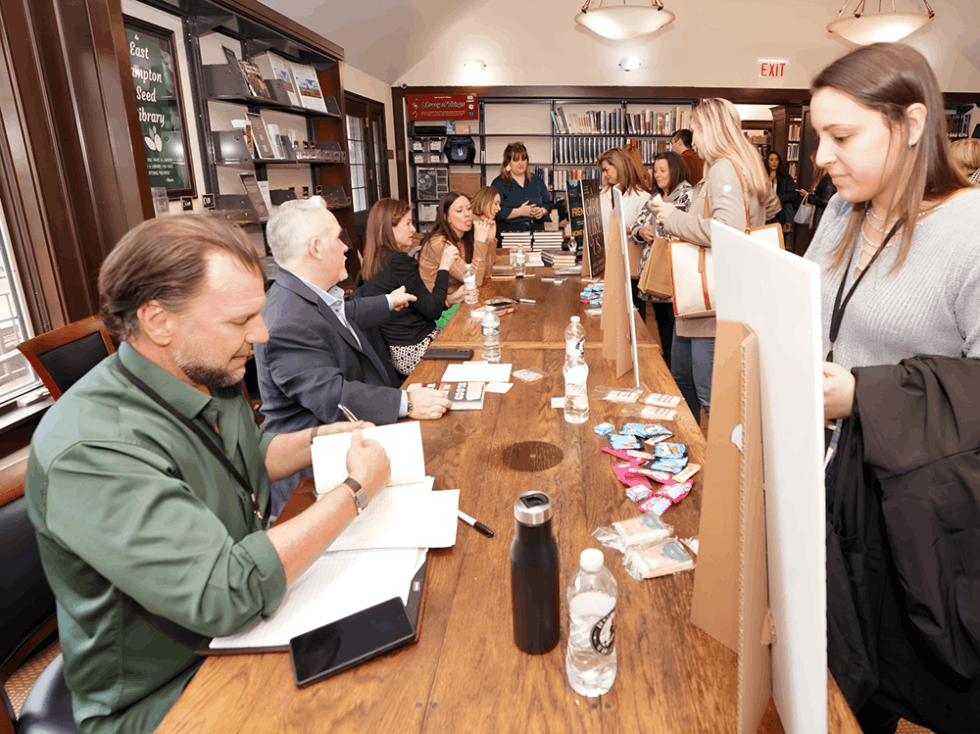 A line up of best selling authors at a long table signing their books for a line of fans