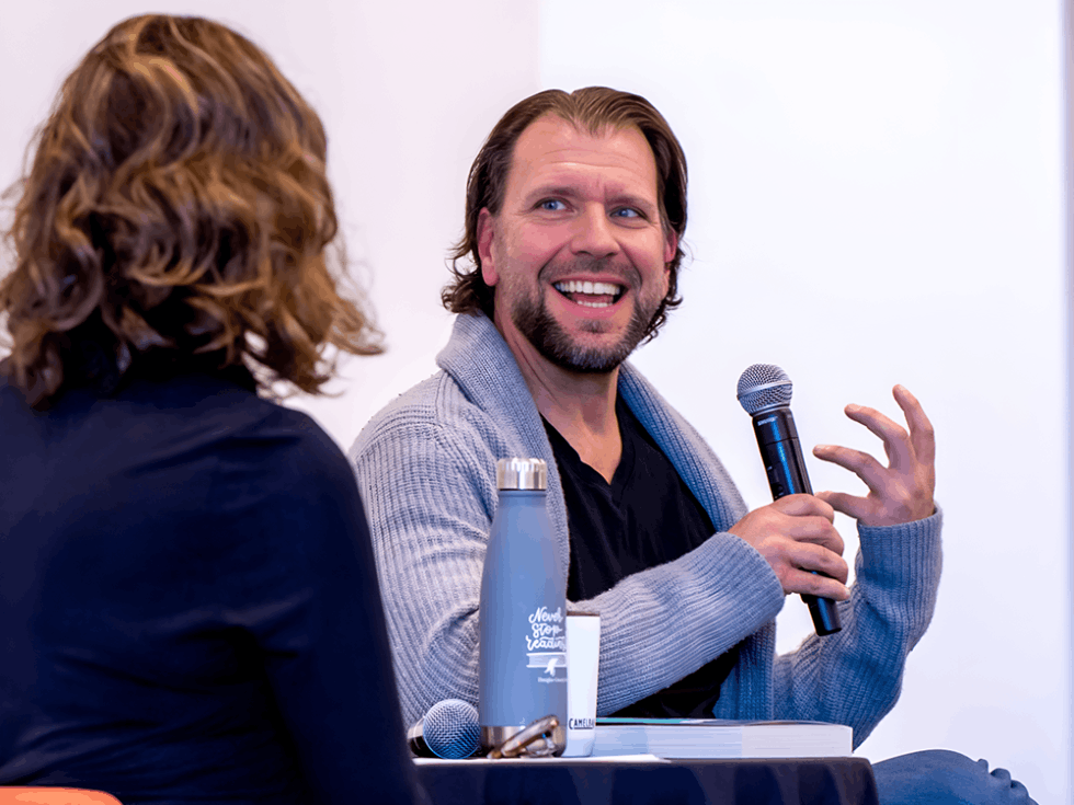 Best-selling author Carter Wilson smiling while speaking into a microphone in a chunky gray cardigan