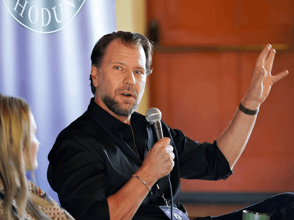 Bestselling author Carter Wilson speaking into a microphone on stage at the Whodunnit Writers conference