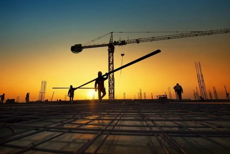 Construction crew and tower crane silhouetted at sunset