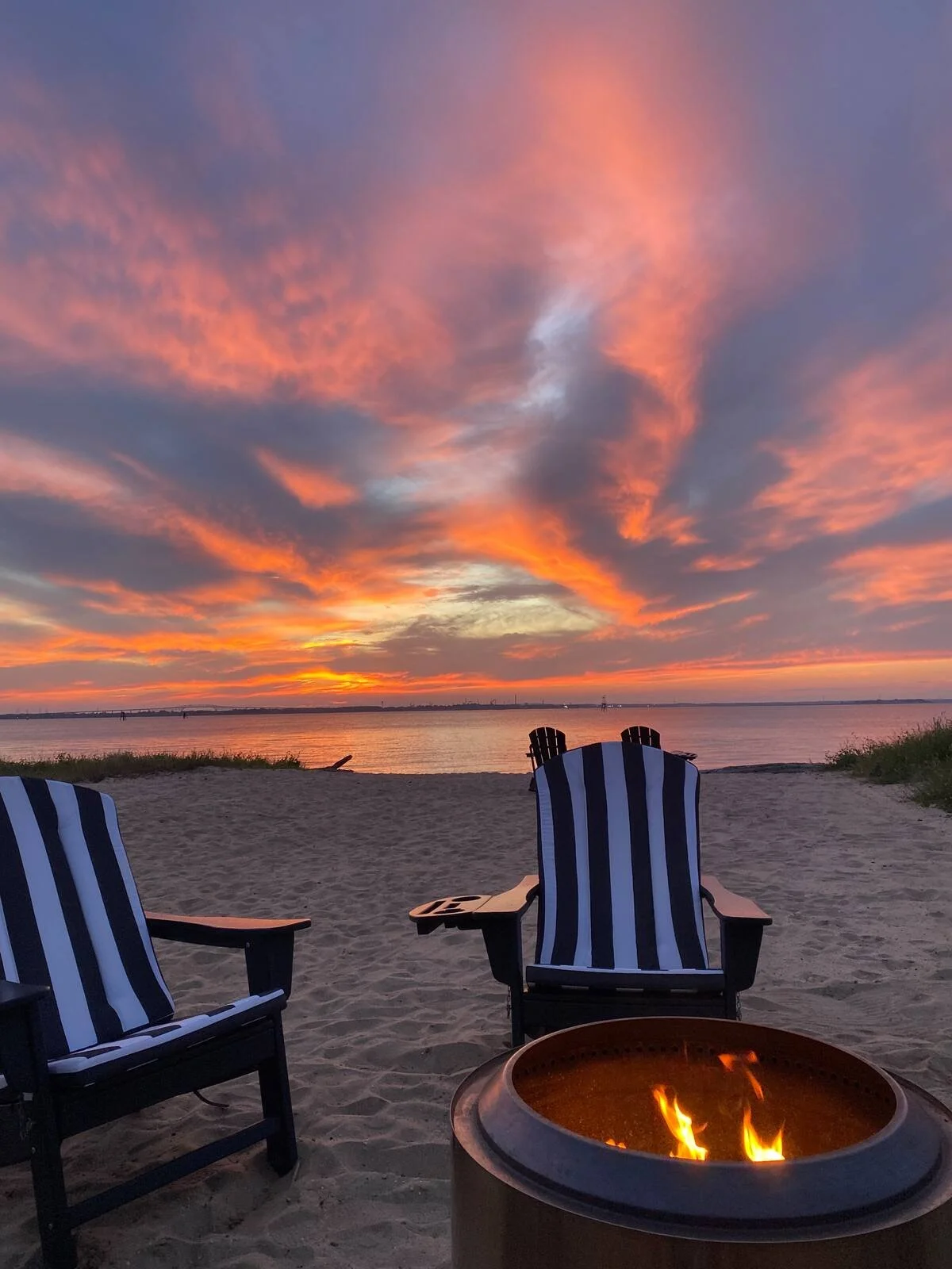 Riverside firepit and striped chairs beneath a vivid sunset