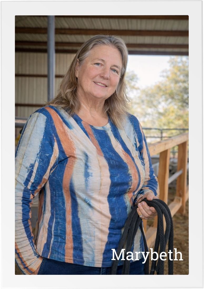 MaryBeth, Founder and Lead Therapist at HorseSpeak, standing in the arena, holding a lead rope and smiling at the camera.