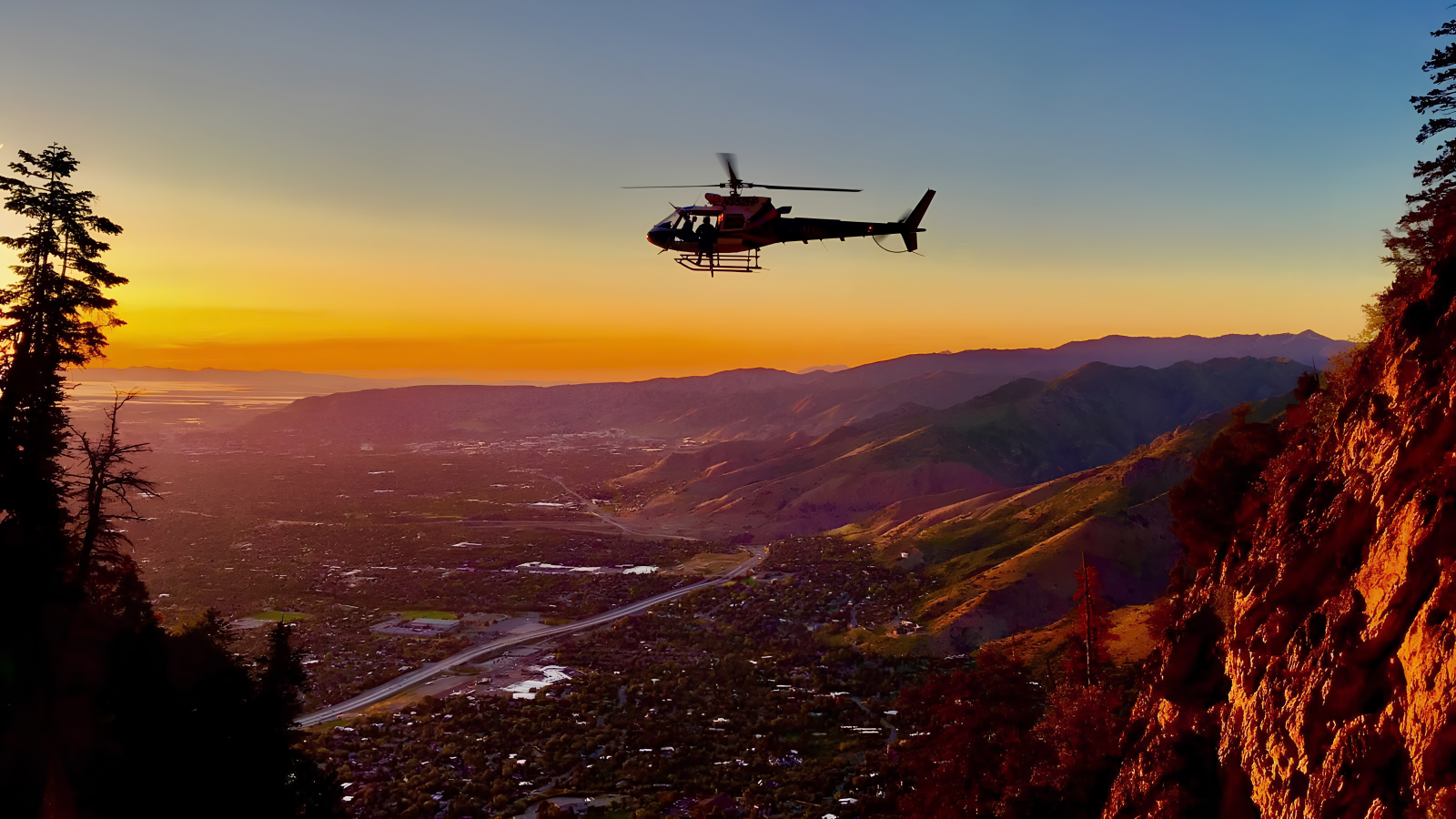 A rescue helicopter flying above the mountains and valley at sunset
