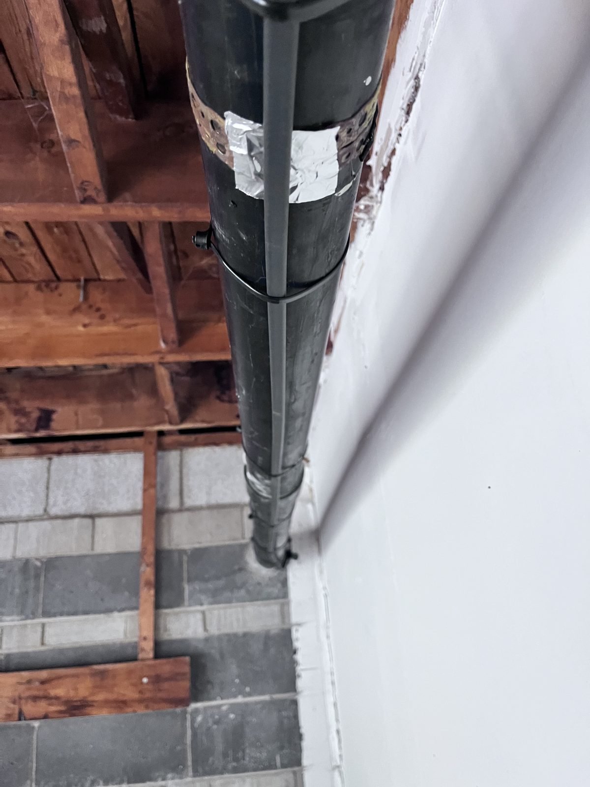 Heating cable running along a vertical pipe beside a basement wall, held with straps