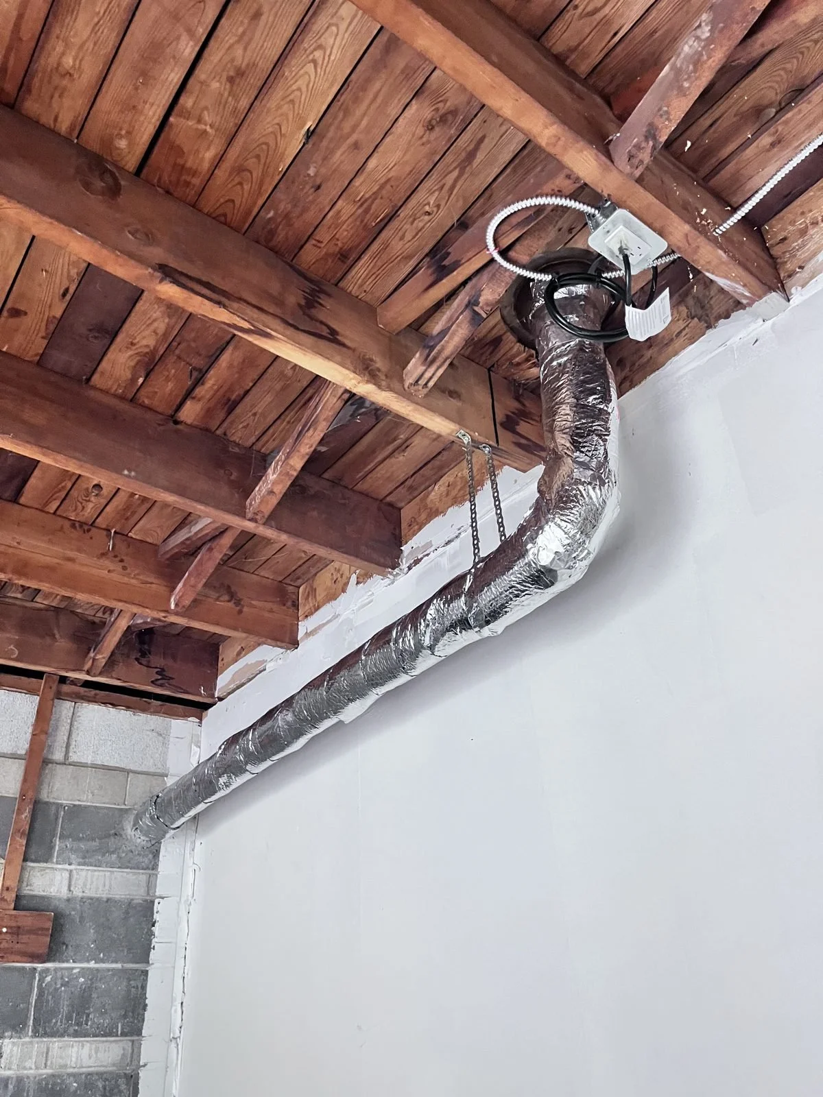 Insulated pipe run along a basement wall under exposed wooden joists