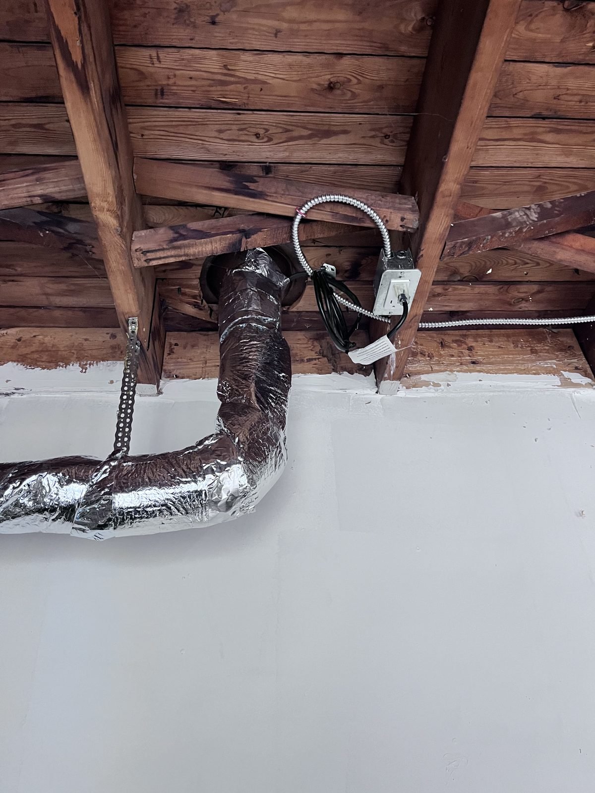 Pipe elbow wrapped in foil-faced insulation with the heating cable plugged into a ceiling outlet
