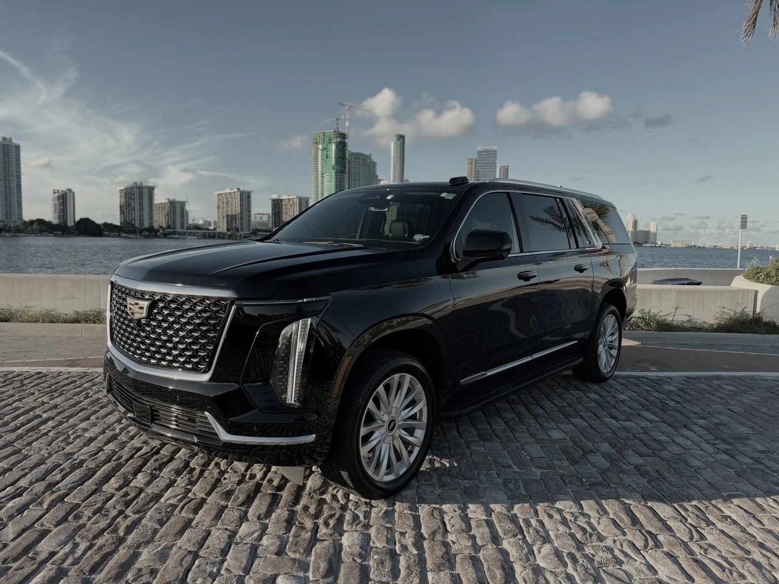 Black Cadillac Escalade beside the water with the Miami skyline behind it