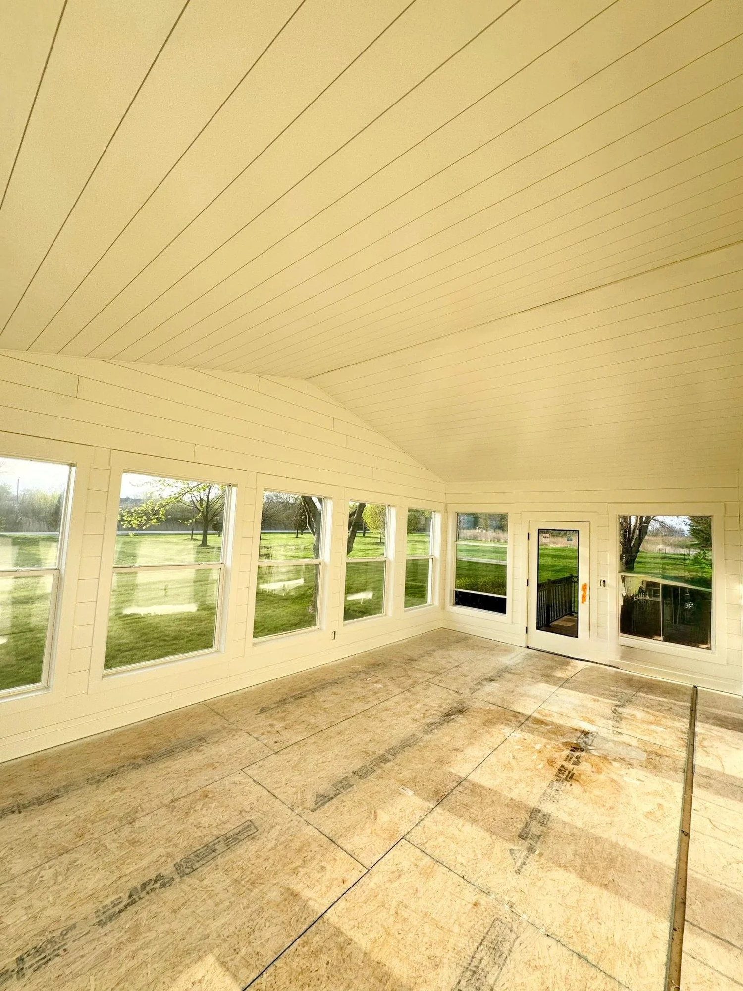 Painted white shiplap sunroom with a long run of windows looking out on a green yard in Grimes, Iowa