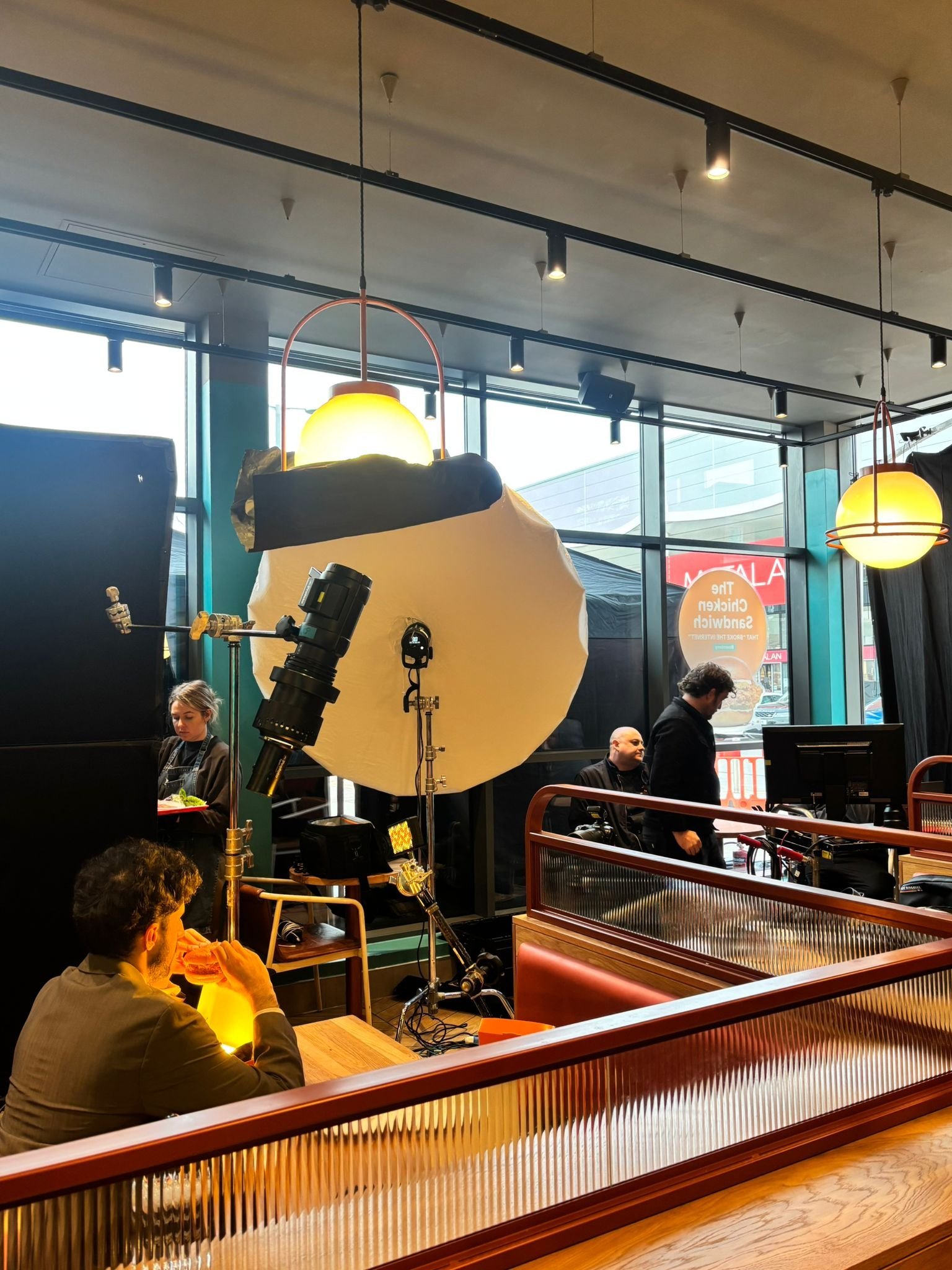 Behind the scenes of Jon Enoch’s Popeyes advertising shoot, with lighting equipment positioned around the restaurant booths.