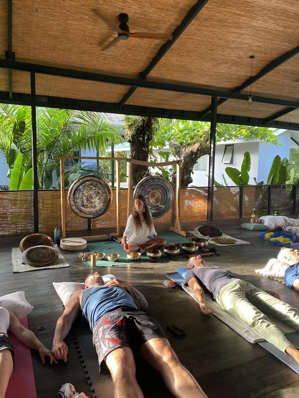 Yoselyn playing singing bowls with guests resting around the gongs