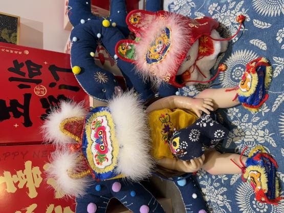 A doll in a tiger hat and tiger shoes, beside a second doll in a red tiger hat, on blue printed cloth