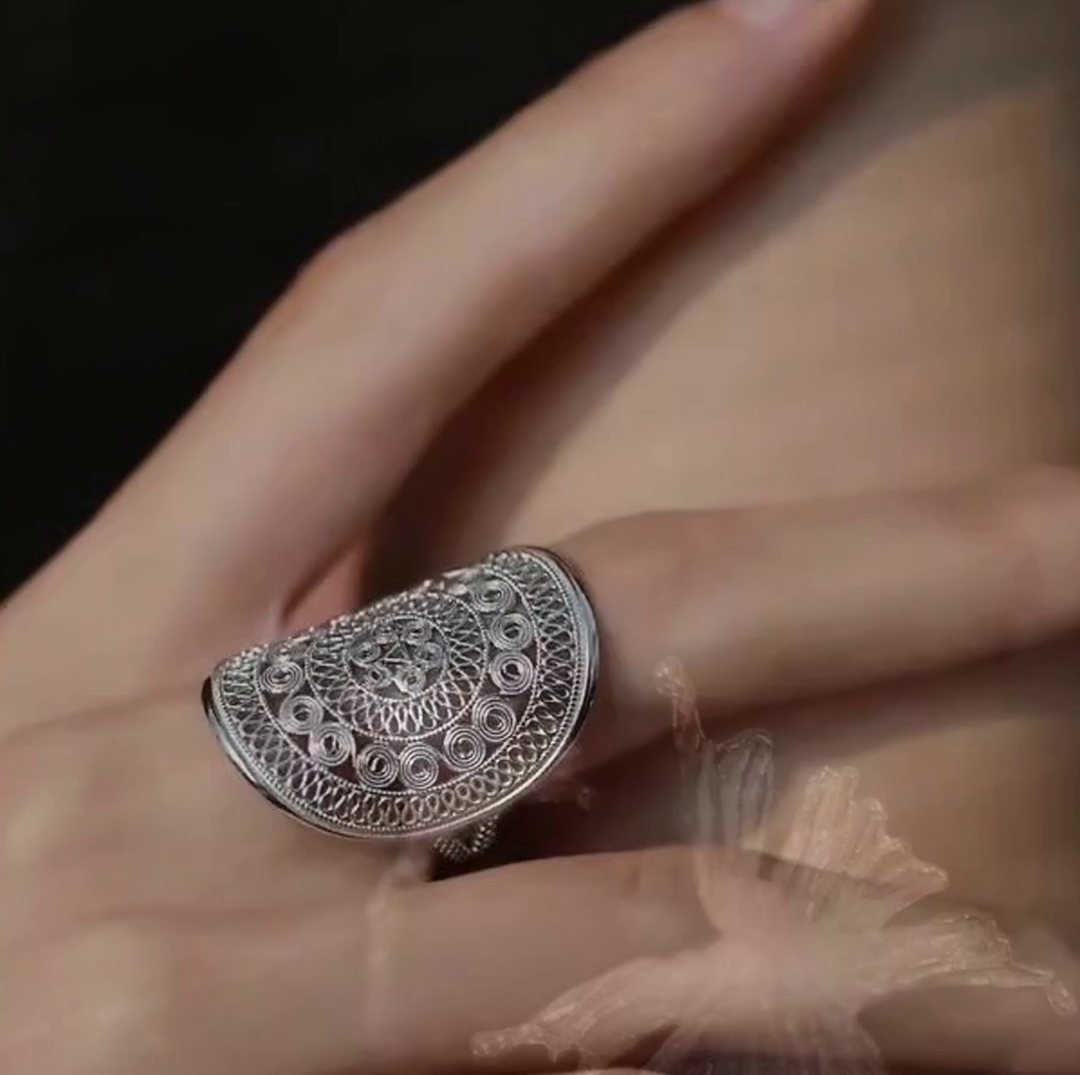 A wide filigree silver ring worn on the hand