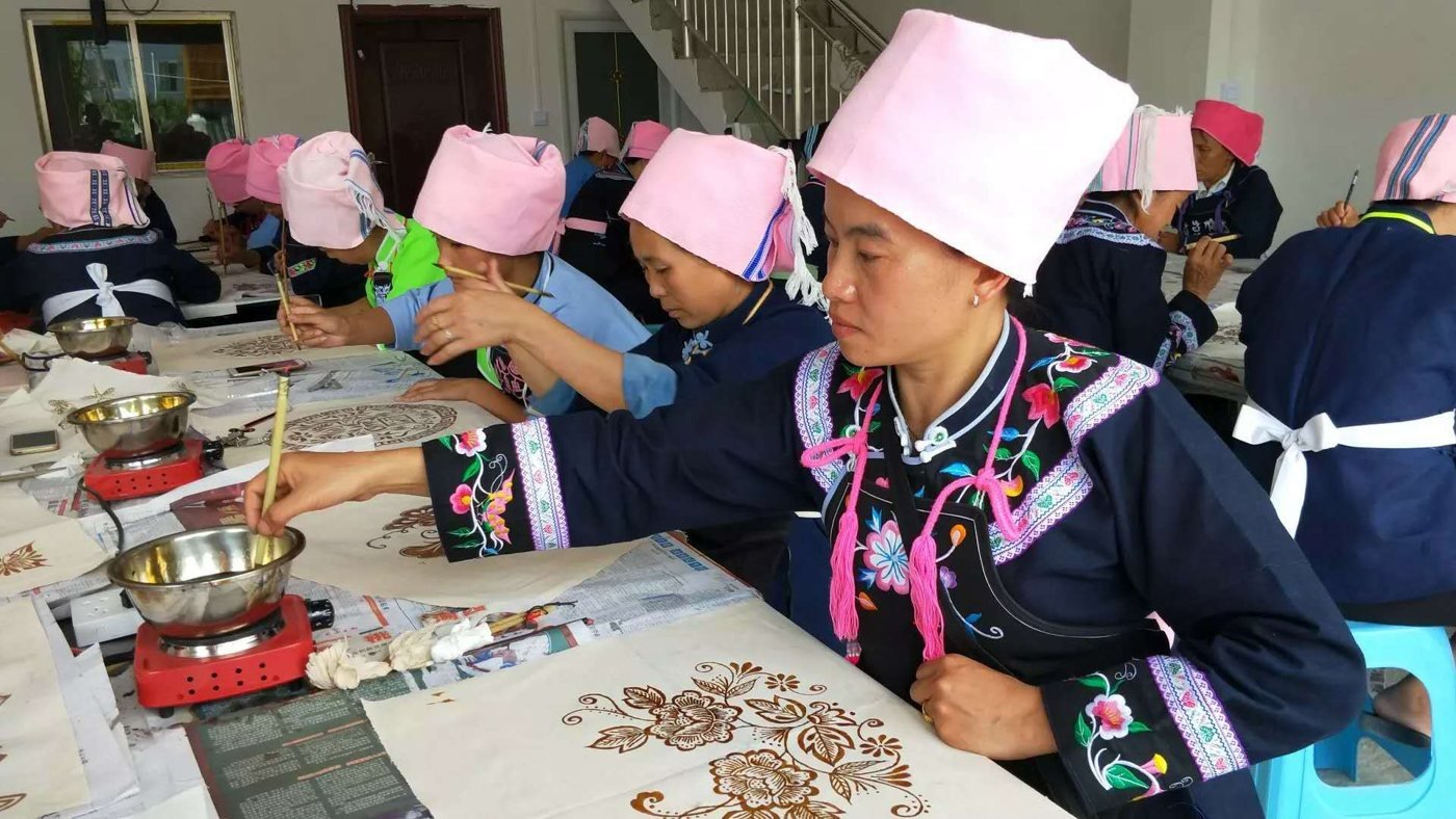 A maker in a pink headscarf paints a floral pattern in hot resin at a training session