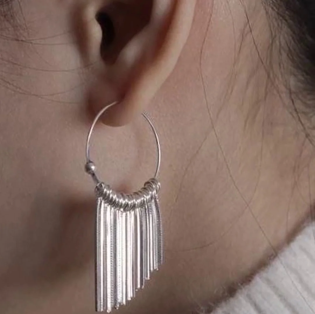 A silver hoop earring with a fringe of fine silver tubes, worn