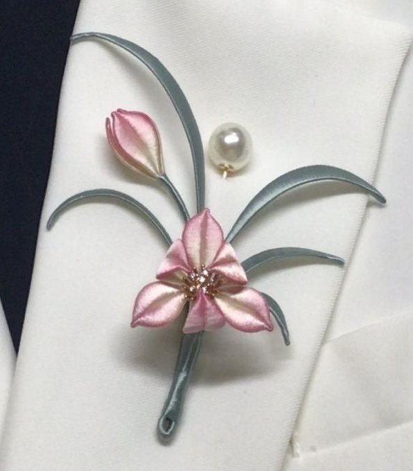 A pink and grey silk flower brooch with a pearl pin on a white lapel