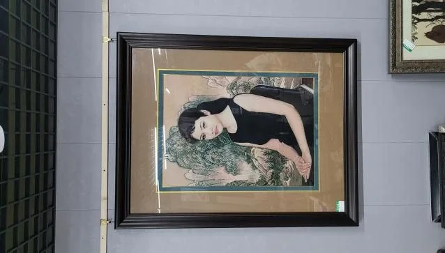 A framed embroidered portrait of a seated woman in a black dress