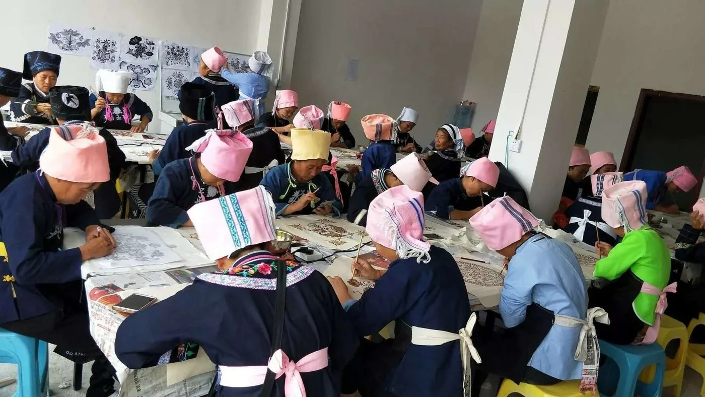 A workshop room filled with makers painting cloth at long tables