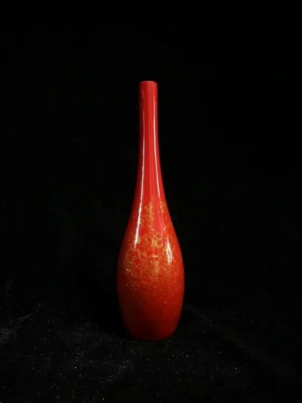 A tall red lacquer vase with a long neck on a black background